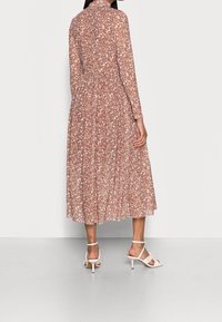 Brun blommig midiklänning med långa ärmar och en rynkad midja. Tyget är lätt och genomskinligt, med ett subtilt blommönster.