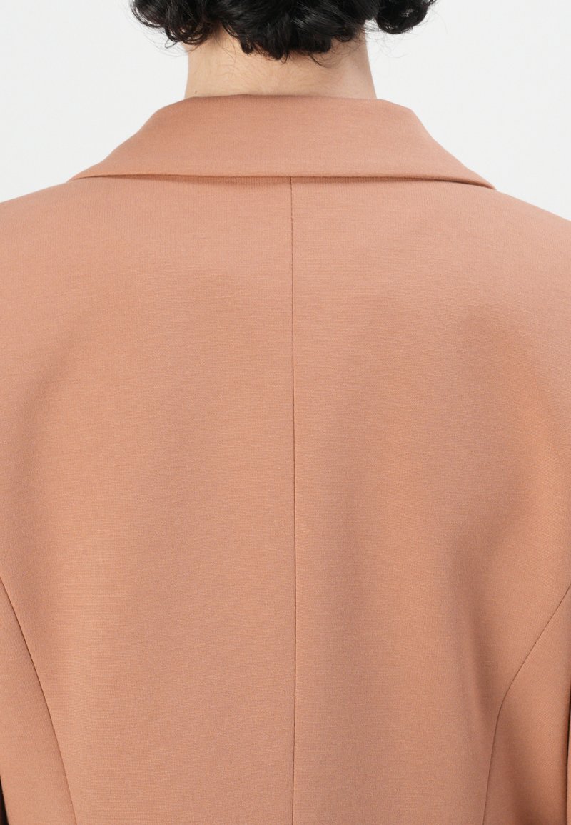 Różowy żakiet z wyraźnym kołnierzem, gładką teksturą i widocznym szwem wzdłuż tylnego szwu.