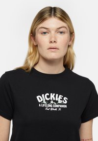 Černé bavlněné tričko s krátkým rukávem a kulatým výstřihem. Obsahuje bílý grafický potisk s textem "DICKIES VĚČNÝ SPOLEČNÍK."