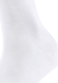 Close-up van een witte enkel sok op een voet, die de gladde, gebreide stofstructuur en het versterkte hielgebied laat zien.