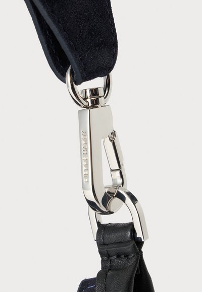 Silver metal clasp engraved with "Pierre Hardy" connecting a black fabric strap to a black leather loop.