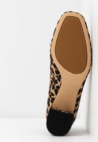 Chaussure à talon haut en imprimé léopard avec un dessus en fourrure texturée, une semelle en caoutchouc tan et noir, et un design à bout pointu.