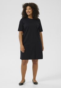 Vestido negro de manga corta, hecho de tela suave, con un corte holgado y un dobladillo a la altura de la rodilla. Diseño sencillo sin patrones ni acentos visibles.