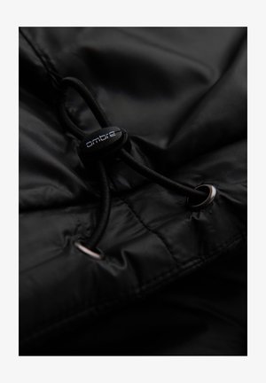 Giacca nera in nylon con cordino di regolazione e un regolatore circolare nero etichettato "ombre". Sono visibili occhielli argentati sul tessuto.