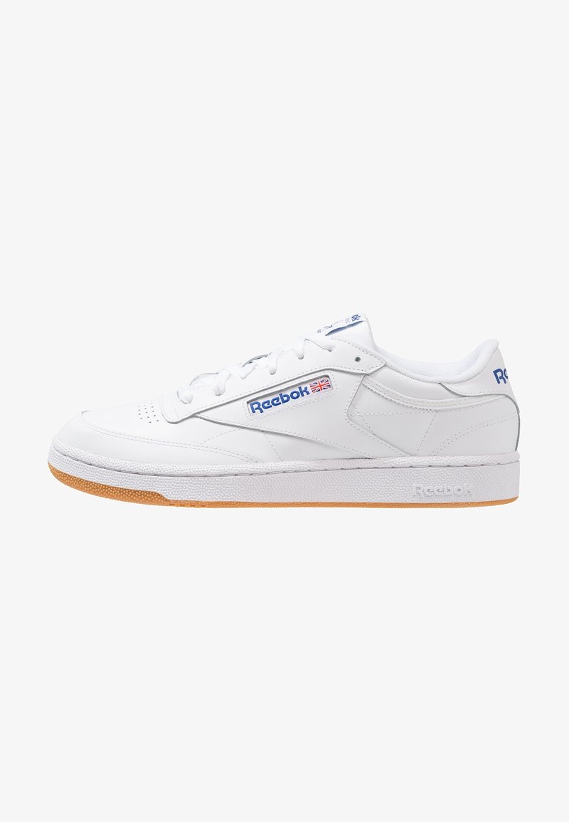 Witte leren sneakers met een laag profiel, geperforeerde teen, blauwe en rode accenten, en een rubberen gumzool. Heeft het Reebok-logo aan de zijkant.