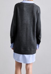 Pullover oversized grigio scuro con bordo a costine, indossato su una camicia colletto azzurro chiaro. Texture morbida e vestibilità rilassata.