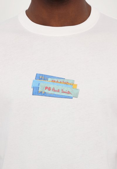 T-shirt blanc avec un design brodé de patchs en tissu colorés dans les tons bleu, vert et jaune, accompagné du texte "PS Paul Smith".