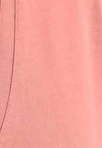 Světle růžová látka s hladkým povrchem, která obsahuje detaily šití a jemný elastický nádech. Detailní záběr zdůrazňuje barvu a strukturu.