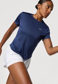 Granatowa sportowa bluzka z krótkim rękawem z materiału odprowadzającego wilgoć; lekkie białe szorty z ukośnym dołem; logo Nike na klatce piersiowej.