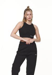 Svart ribbet crop topp med høy hals, parret med svarte joggebukser med elastisk midje og logo detalj på siden.