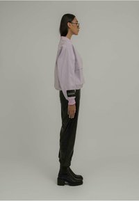 Lilla genser med en cropped design og lomme, kombinert med svarte tapered bukser og chunky svarte boots med hæl.