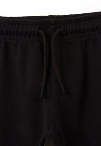Schwarze Jogginghose mit Kordelzug, Gummibund, weichem Stoff und glatter Textur. Die Enden der Kordelzüge haben schwarze Spitzen.