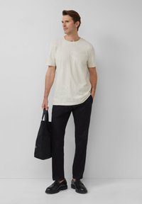 Lichtgekleurde T-shirt met korte mouwen en subtiele patronen, gecombineerd met zwarte broek en een tote bag. Zwarte schoenen maken de outfit compleet.