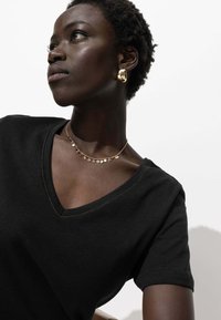 T-shirt noir en col en V avec des manches courtes et des coutures jaunes contrastantes. Porté avec un délicat collier en or et des boucles d'oreilles créoles.