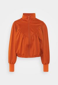 Chaqueta naranja con cremallera, cuello alto y hombros fruncidos. Tejido suave, de longitud corta y con puños ajustados. Textura lisa.