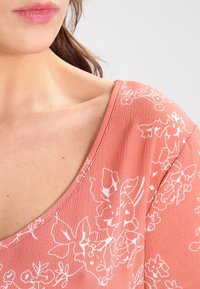 Haut pêche à motifs floraux avec un col en arrondi et des manches courtes, orné de motifs de fleurs blanches sur un tissu texturé.