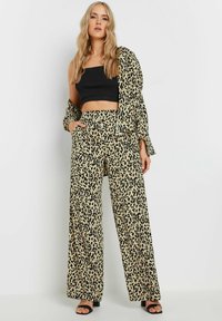 Beige luipaardmotief co-ord set met een cropped top en wijde broekspijpen, vervaardigd uit een lichtgewicht stof en voorzien van zwarte accenten.