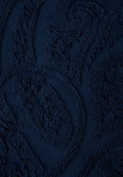 Tissu texturé bleu foncé avec motifs abstraits de feuilles et géométriques en relief dans un style de fil bouclé.