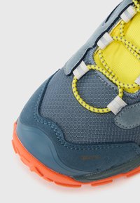 Zili sporta apavi ar teksturētu auduma augšdaļu, dzelteniem akcentiem un oranžu gumijas zoli, ar elastīgām šņorēm un zamša elementiem.