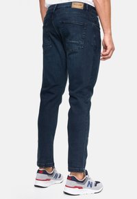 Donkerblauwe spijkerbroek met een slim-fit ontwerp, middelhoge taille en zichtbare stiksels. Voorzien van twee achterzakken en een leren merkpatch.