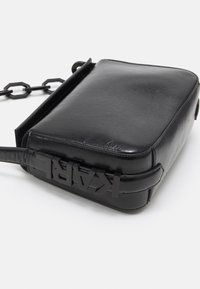 Czarna skórzana torebka na ramię z łańcuszkowym paskiem i przednim paskiem z wytłoczonymi literami piszącymi "KARL" w kolorze czarnym.