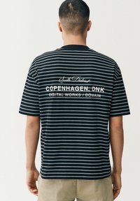 Sort og hvid stribet t-shirt lavet af bomuld, med et rygmotiv der har brandingtekst i kontrastfarve hvid, korte ærmer og en afslappet pasform.