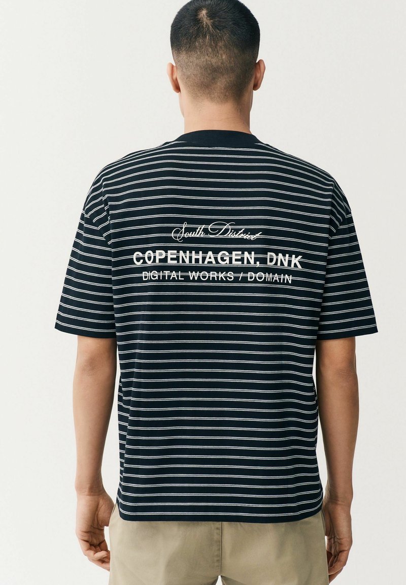Sort og hvid stribet t-shirt lavet af bomuld, med et rygmotiv der har brandingtekst i kontrastfarve hvid, korte ærmer og en afslappet pasform.