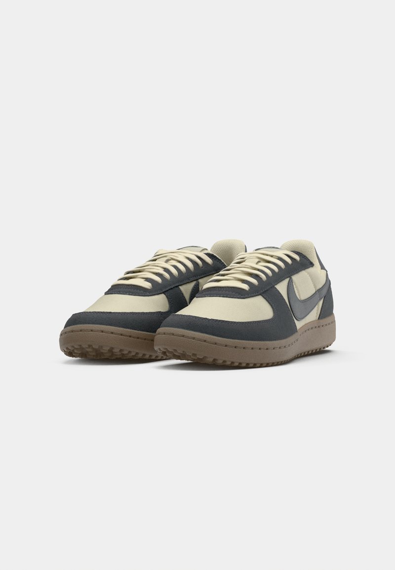 Sneakers met een beige mesh bovenwerk en donkerblauwe suède overlays, met een rubberen zool met een gestructureerd oppervlak en beige veters.