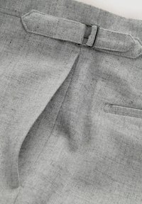 Pantalones grises hechos de tejido texturizado, con un pliegue central, un cinturón con una hebilla metálica y un pequeño bolsillo lateral.