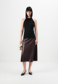 Black sleeveless top with a fitted design, paired with a burgundy leather midi skirt and pointed-toe black heels; holds a beige handbag.