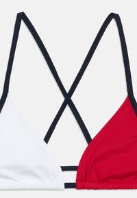 Κόκκινο και λευκό τρίγωνο τοπ μπικίνι με ναυτικό μπλε τιράντες. Διαθέτει σταυρωτές τιράντες στην πλάτη και λεία υφή υφάσματος. Χωρίς επιπλέον σχέδια ή διακοσμητικά στοιχεία.