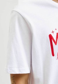 Witte katoenen t-shirt met een rood bedrukt grafisch ontwerp op de voorkant, korte mouwen en een zachte, gladde textuur.