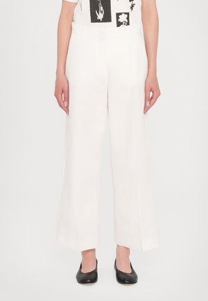 Mujer vistiendo pantalones blancos de tiro alto y pierna ancha combinados con zapatos planos negros y una camiseta blanca con estampado gráfico.