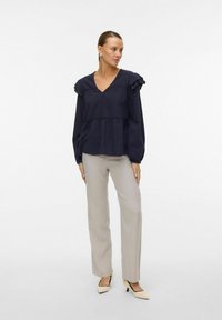 Blusa blu navy con spalle arricciate, scollo a V e design a strati. Abbinata a pantaloni beige chiaro e décolleté a punta.