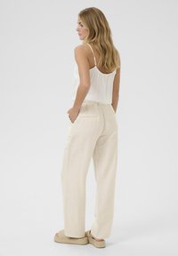 Haut blanc à fleurs sans dos, pantalon en lin beige clair avec poches latérales et sandales espadrilles tissées. Design simple et fluide, et texture naturelle.
