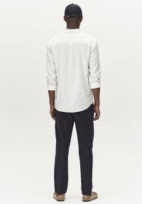 Bela lanena srajca z dolgimi rokavi, mornarsko modri hlače in mornarsko modra kapa. Srajca ima hrbtno jermenico in zavihane manšete, medtem ko so čevlji bež.