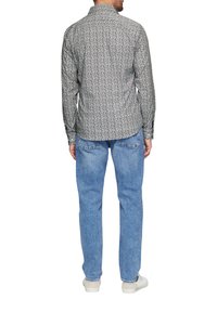 Schwarze und weiße Bluse mit Blumenmuster, getragen mit hellblauen Jeans und weißen Sneakers, von hinten aufgenommen.