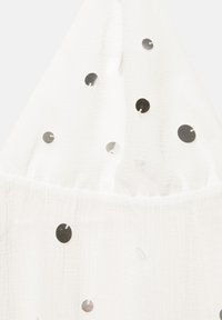 Tissu blanc texturé avec de petites sequins ronds argentés éparpillés cousus sporadiquement sur toute la surface.