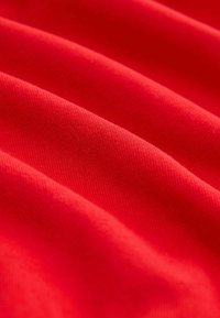 Tela roja con una textura suave, que presenta un ligero estiramiento y un patrón acanalado visible, dispuesta en suaves ondas.