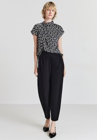 Blouse à motifs noir et blanc à manches courtes, associée à un pantalon noir taille haute et des chaussures noires à bout pointu.