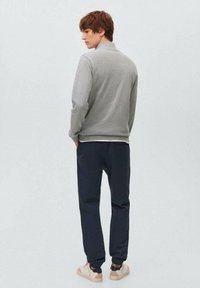 Grå zip-up sweatshirt med hög krage, som matchas med mörkblå avsmalnande byxor. Beiga sneakers med mörka accenter fulländar looken.