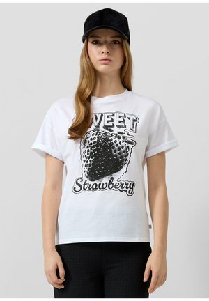 Jeune femme portant une casquette noire et un t-shirt blanc avec un grand graphique de fraise noire et le texte « Sweet Strawberry ».
