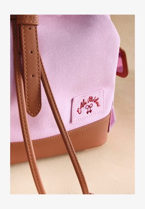 Geantă roz din pânză cu bază sintetică maro, având o curea maro și un patch brodat cu logo. Textură netedă cu accente minimale.