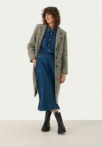 Manteau en pied-de-poule gris et blanc sur une chemise en denim bleue et une jupe. Des bottines noires à talons épais complètent l'ensemble.
