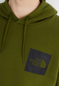 Oliwkowa bluza z miękkiego materiału, z granatowym kwadratowym logo na lewej piersi z białym napisem oraz kapturem ze sznurkiem.