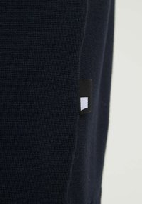 Maglione a maglia di colore blu navy con tessuto texturizzato. Presenta un piccolo etichetta nera con un accento rettangolare bianco sul lato.