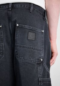 Dark denim cargo shorts with two back pockets, featuring a black label with logo and silver hardware accents. Textured fabric with visible stitching.