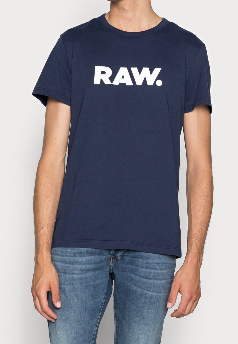 Navy blue cotton t-shirt with short sleeves featuring a large white "RAW." logo prominently displayed on the front.