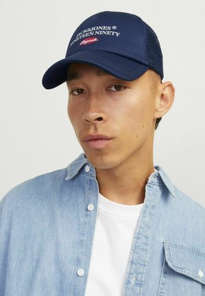 Gorra de béisbol azul marino con pico curvado, que presenta el logo en texto blanco "Jack&Jones Nineteen Ninety." Los paneles laterales de malla mejoran la transpirabilidad.