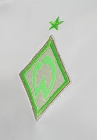 Weißer Stoff mit einem grünen und hellgrünen gestickten Logo in Form eines Diamonds, akzentuiert von einem kleinen grünen Stern darüber.